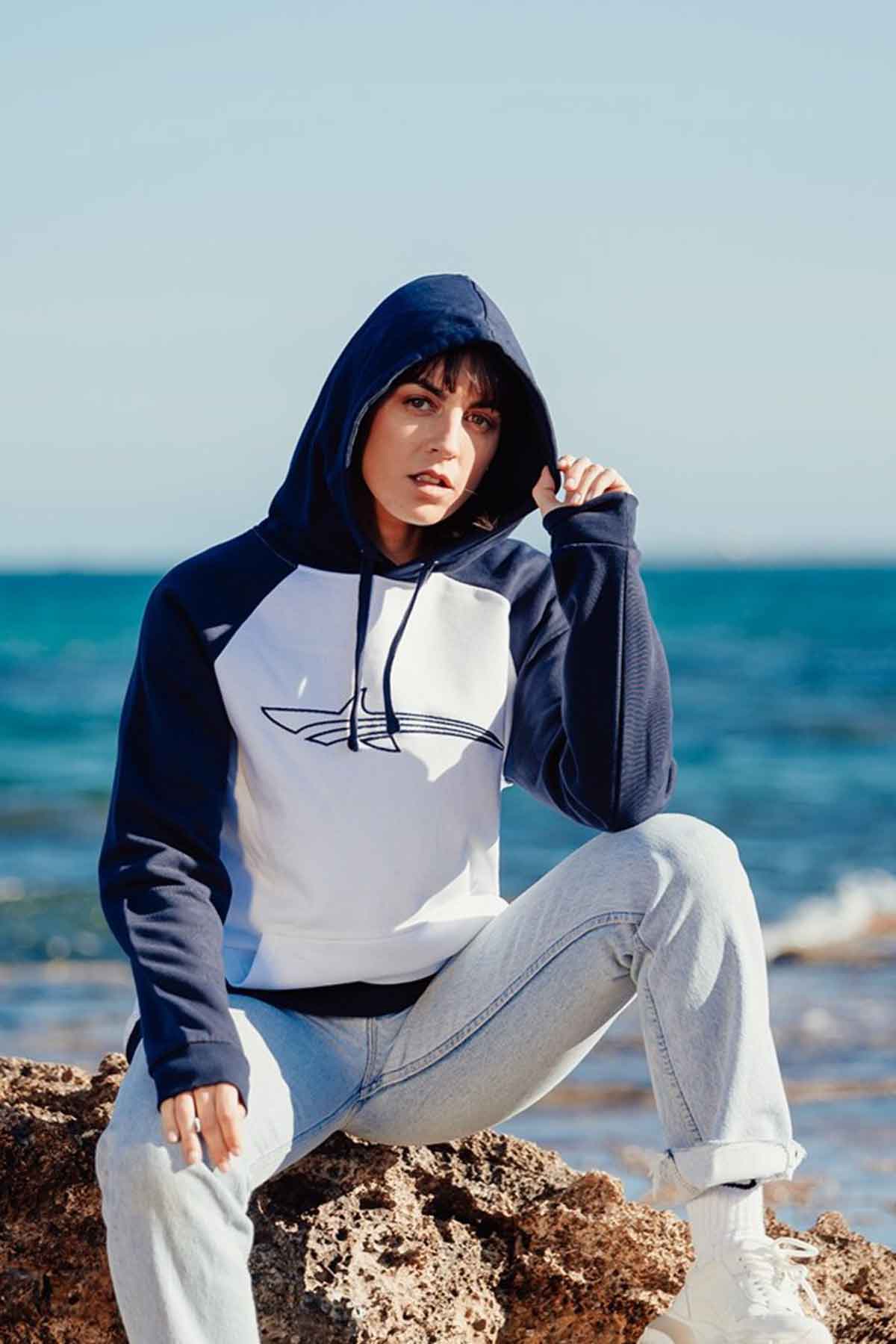 woman sitting at the beach wearing a white and blue hoodie from oceanman
