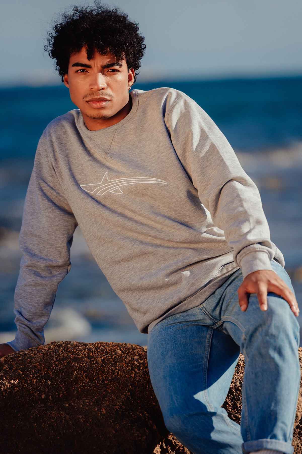 man sitting at the beach wearing a bali edition grey sweater
